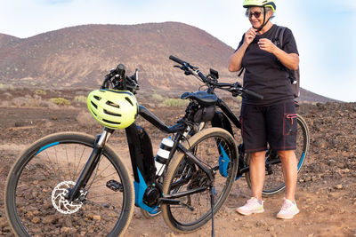 Full length of woman standing by bicycles against mountain and sky