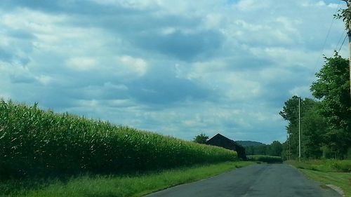 Road passing through field against cloudy sky