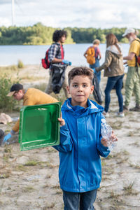 Boy collects garbage plastic waste on the shore of a lake together with his volunteer friends