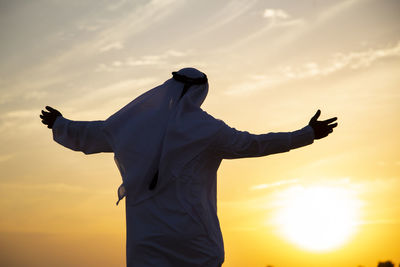 Rear view of man in traditional clothing standing against sky during sunset
