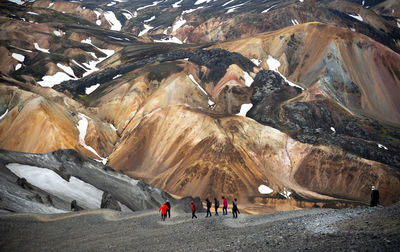 A group of hikers walking down a mountain with colorful volcanic mountains in the background.