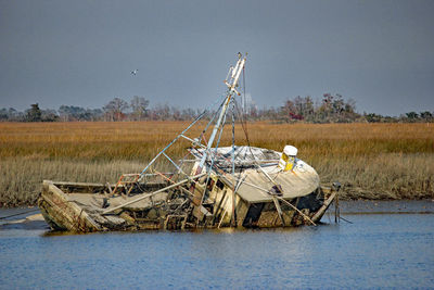 Abandoned boat on field by lake against sky