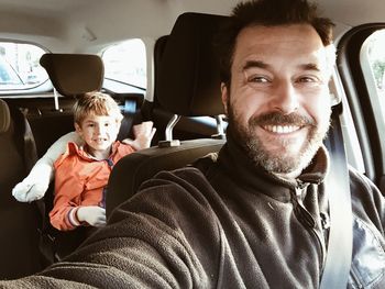 Smiling father in car with son sitting at back seat