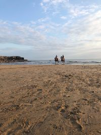 Women riding horse at beach against cloudy sky