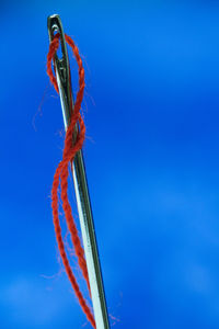 Close-up of sewing needle and thread against blue background