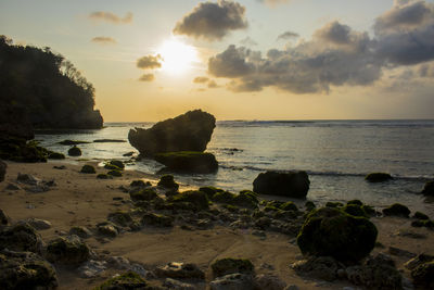 Rocks on beach against sky during sunset