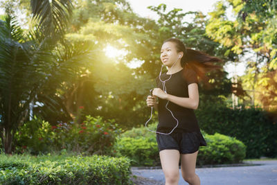 Young woman listening music while running on footpath in park