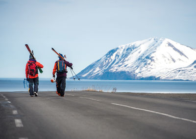 Two men walking on a paved road in iceland with mountains and water