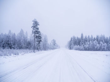 Empty road along snow covered trees against sky