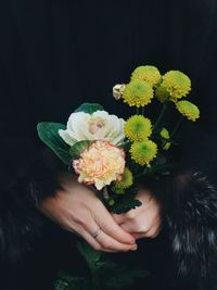 Cropped image of woman holding flowers against black background