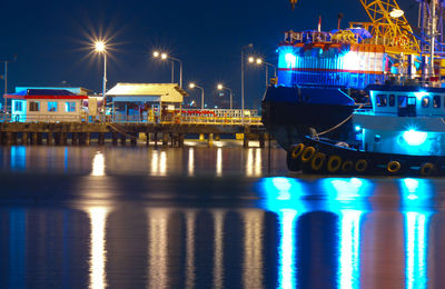 Illuminated boats moored at harbor against sky at night