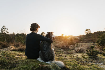 Rear view of woman with dog sitting outdoors