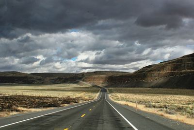 Empty road leading towards mountains against cloudy sky