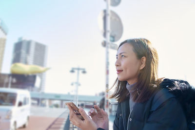 Woman using mobile phone in city against sky