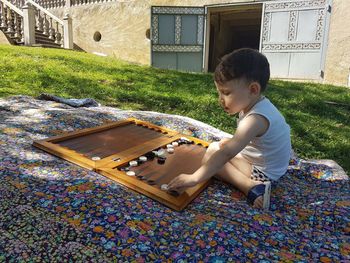 Side view of boy playing with toys while sitting on blanket in yard