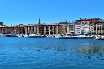 Sailboats in sea by buildings against clear blue sky