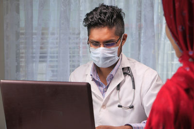 Close-up of doctor wearing flu mask sitting at clinic