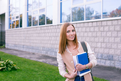 Portrait of smiling young woman holding books while standing on field