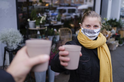 Portrait of woman wearing mask holding coffee cup while standing outdoors