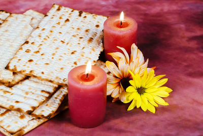 Close-up of illuminated candles with flowers and roasted crackers on fabric