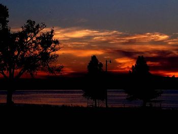 Silhouette trees by lake against sky during sunset