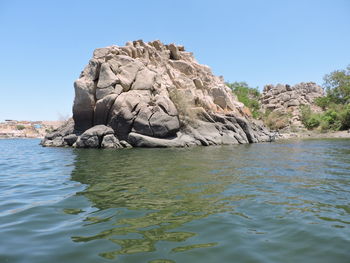 Rock formation in sea against clear blue sky