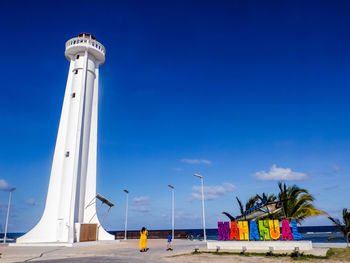 Low angle view of lighthouse by building against blue sky