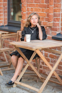 Full length of young woman sitting on table at cafe
