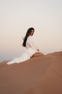 Portrait of young woman standing on sand at desert 