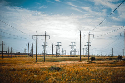 Electricity pylons on field against sky