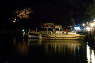 Boats moored on river against illuminated sky at night