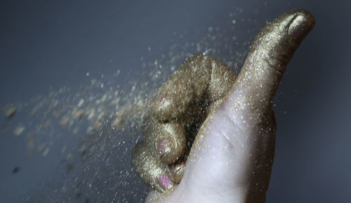 Cropped image of hand with gold glittering powder paint against gray background