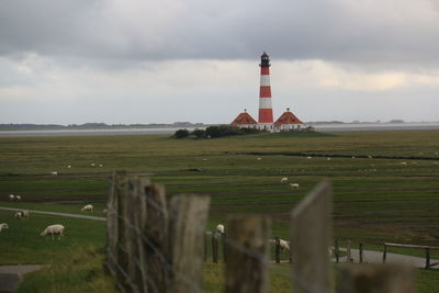 Lighthouse on field against cloudy sky