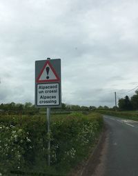 Road sign on country road against cloudy sky