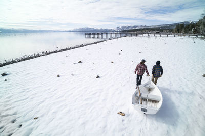 Two men pull a white rowboat across a snowy shore in south lake tahoe, ca