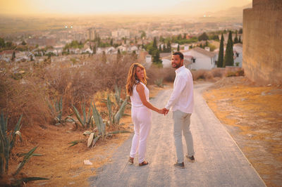 Full length of young couple on dirt road in city at sunset