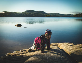 Girl standing on rock by lake against sky
