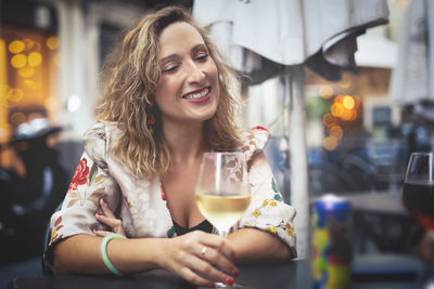 Smiling woman having wine while sitting at table in restaurant