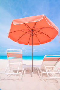 Deck chairs and parasols on beach against blue sky