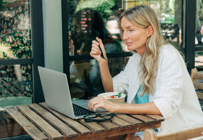 A woman has breakfast in a cafe and works remotely using a laptop.