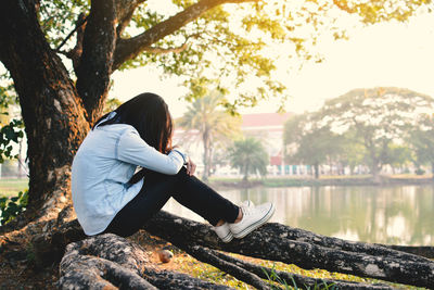 Woman sitting on fallen tree by lake