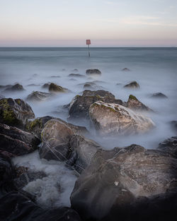 Scenic view of sea against sky during sunset with waves moving over rocks 