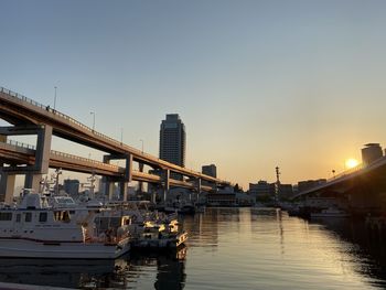 Bridge over river in city against clear sky during sunset