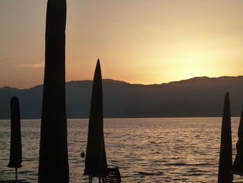 Silhouette wooden posts in sea against orange sky