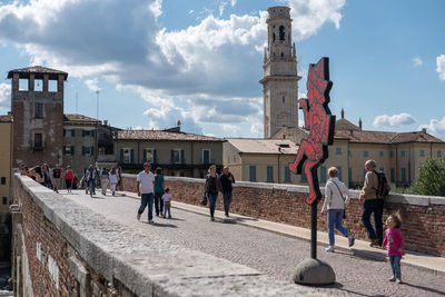 People walking by buildings in city against sky