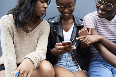 Three friends sitting side by side looking at cell phone