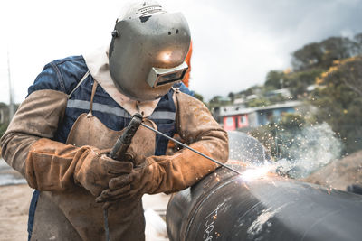 Midsection of man working at shore welding a pipe