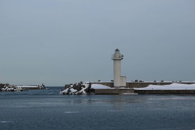 Lighthouse by sea against clear sky