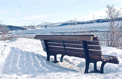 Empty bench on snow covered park against sky