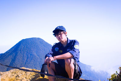 Young man sitting on mountain against clear sky